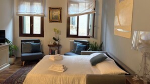 Una camera da letto con un letto grande, due comodini, una sedia, un termosifone e una finestra con tende leggere.