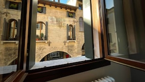 Vista da una finestra di un edificio con facciata in pietra, diverse aperture e un camino ben visibile.