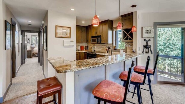 A modern kitchen with a granite countertop, bar stools, pendant lights, and a view of the outdoors. - Platinum Frost Fire, Hot Tub access, Near Slopes! (Keystone)