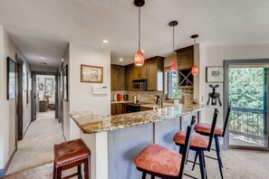 A modern kitchen with a granite countertop, bar stools, pendant lights, and a view of the outdoors. - Platinum Frost Fire, Hot Tub access, Near Slopes! (Keystone)