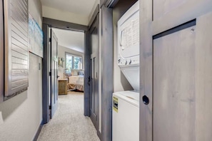 A laundry room with a washer and dryer, a door leading to a bedroom, and a hallway with a carpeted floor.