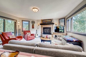 A spacious living room with a fireplace, large windows, and comfortable seating.