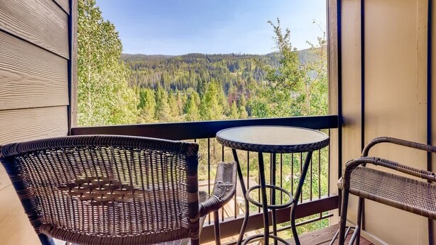 A balcony with wicker chairs and a small round table, overlooking a forested landscape. - Platinum Frost Fire, Hot Tub access, Near Slopes! (Keystone)