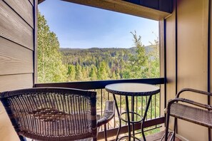 A balcony with wicker chairs and a small table, overlooking a forested landscape.