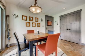A dining area with a wooden table, four chairs, and a chandelier. There are framed pictures on the wall and a door with a sign. - Platinum Frost Fire, Hot Tub access, Near Slopes! (Keystone)