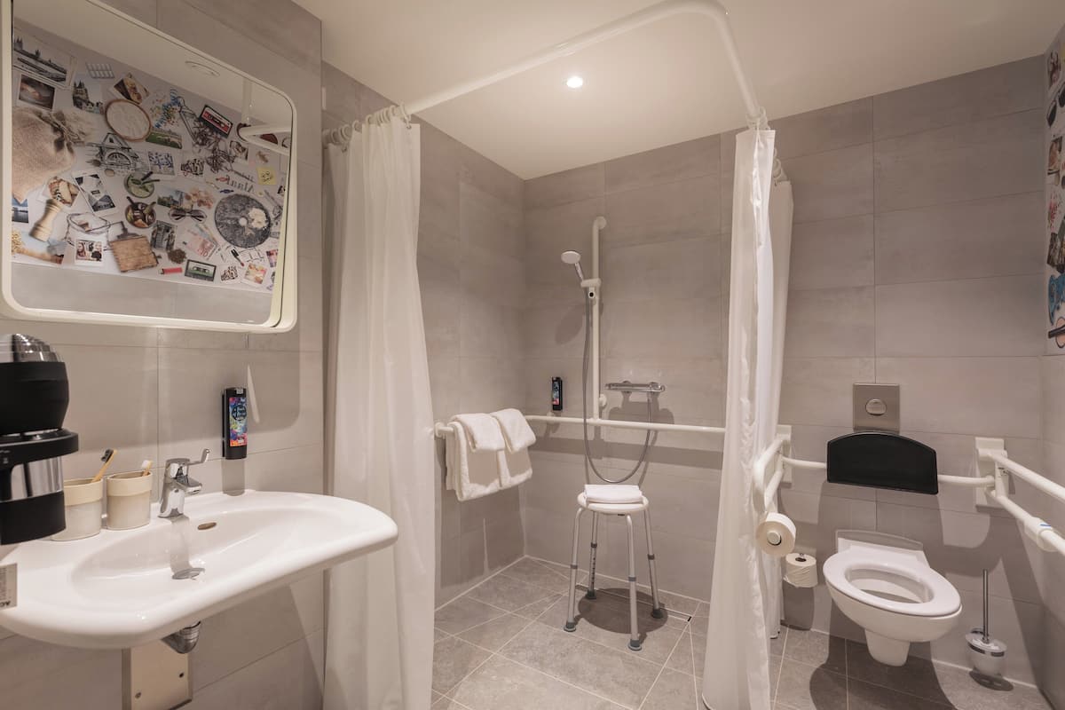 A bathroom with a sink, toilet, shower, and a mirror with a wall decal.
