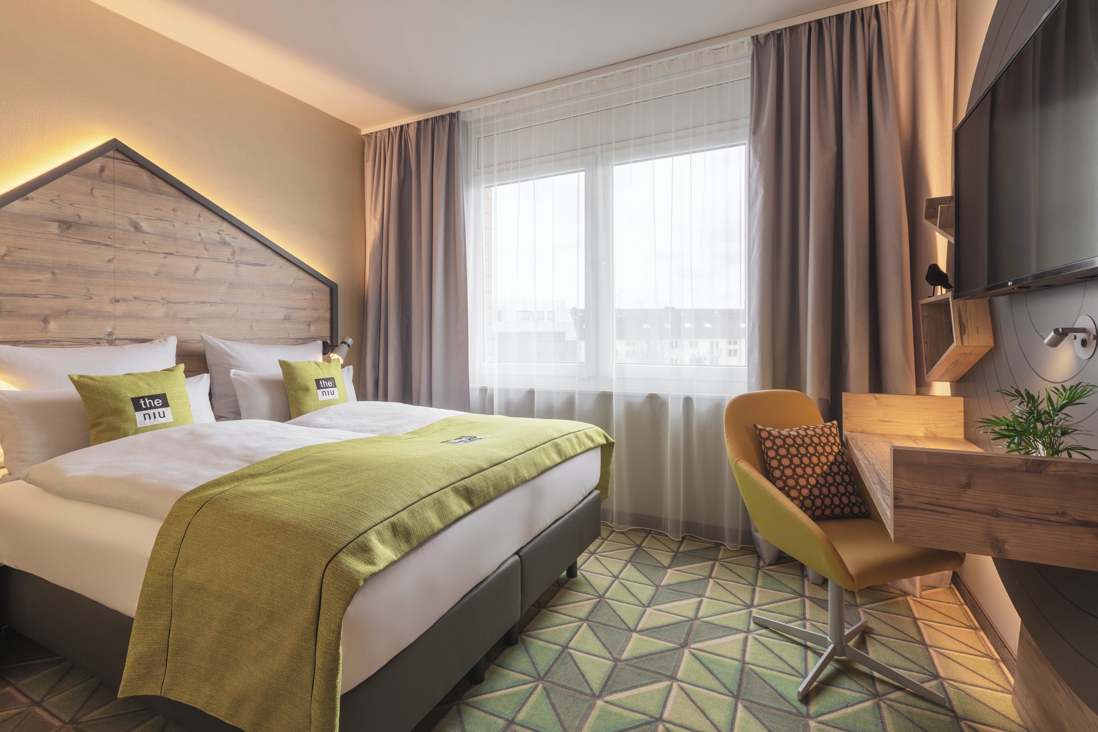 A hotel room with a bed, a desk, a chair, and a large window with curtains.