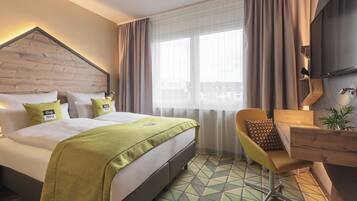 A hotel room with a bed, a desk, a chair, and a large window with curtains.