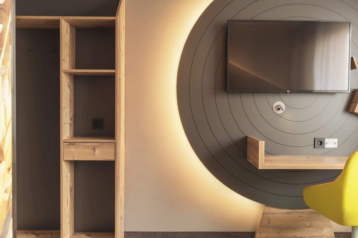 A modern room with a built-in wooden shelving unit, a flat-screen TV mounted on a circular wall, and a yellow chair.