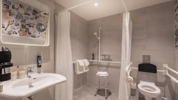 A bathroom with a sink, toilet, shower, and a mirror with a wall decal.