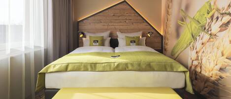 Habitación de hotel con cama, un banco, cabecera con detalles de madera y una pared con una planta grande.