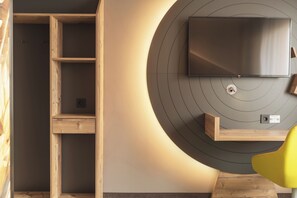 A modern room with a built-in wooden shelving unit, a flat-screen TV mounted on a circular wall, and a yellow chair. - Holiday Inn – the niu, Mill Cologne Mülheim by IHG (Cologne)