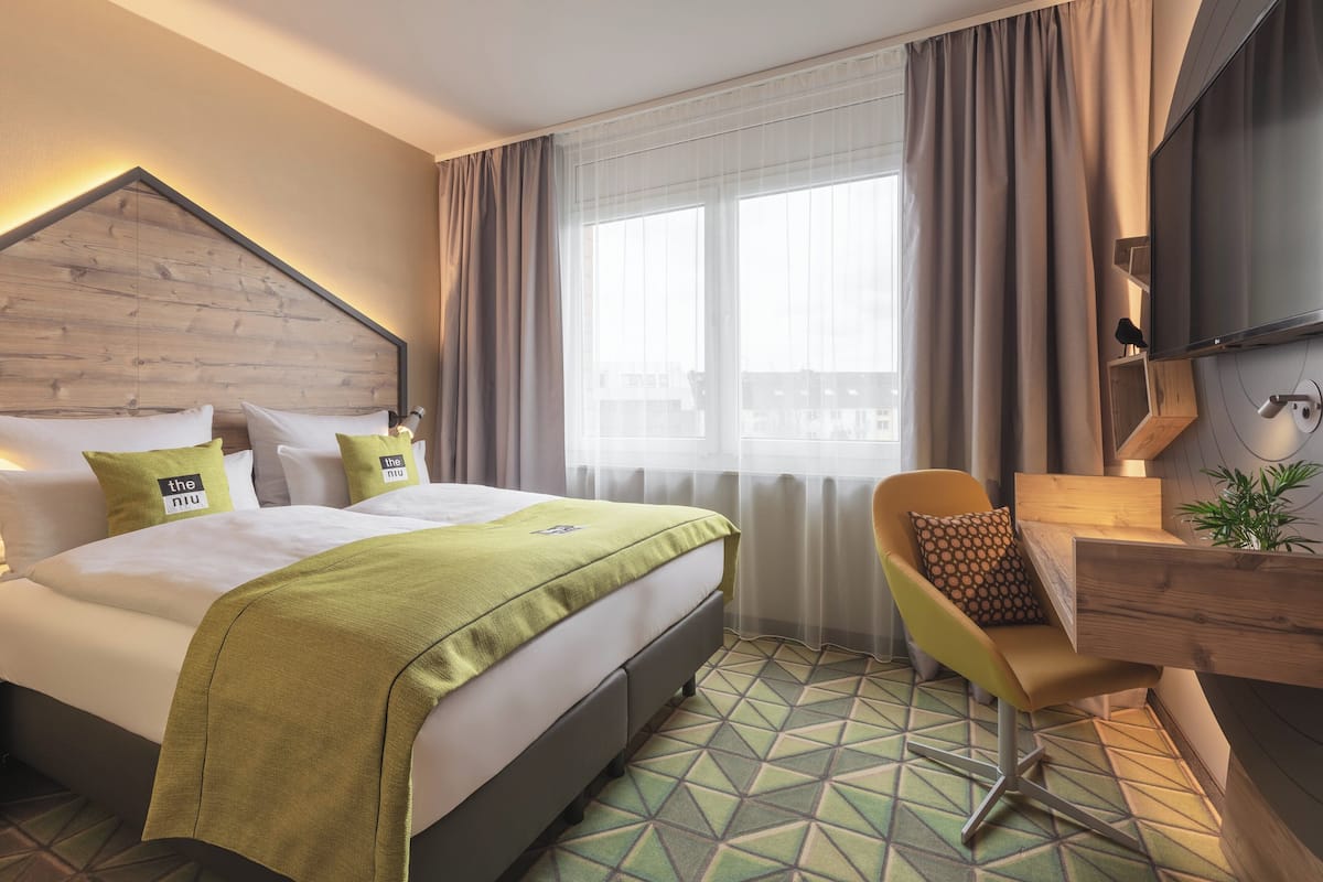 A hotel room with a bed, a desk, a chair, and a large window with curtains.