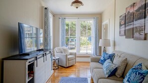 A living room with a sofa, a TV, a small table, and a window with curtains. - Saltbox - Pacific Grove House - Two Blocks to Beach and Downtown! (Pacific Grove)