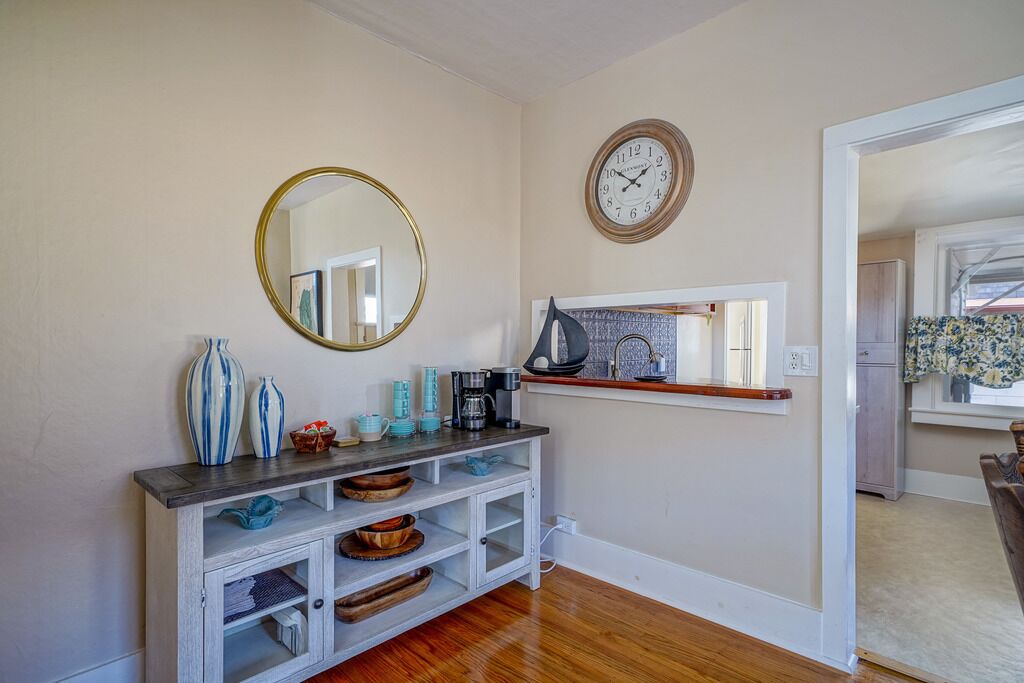 A well-lit entryway with a wooden console table, a round mirror, a wall clock, and a small shelf with decorative items.