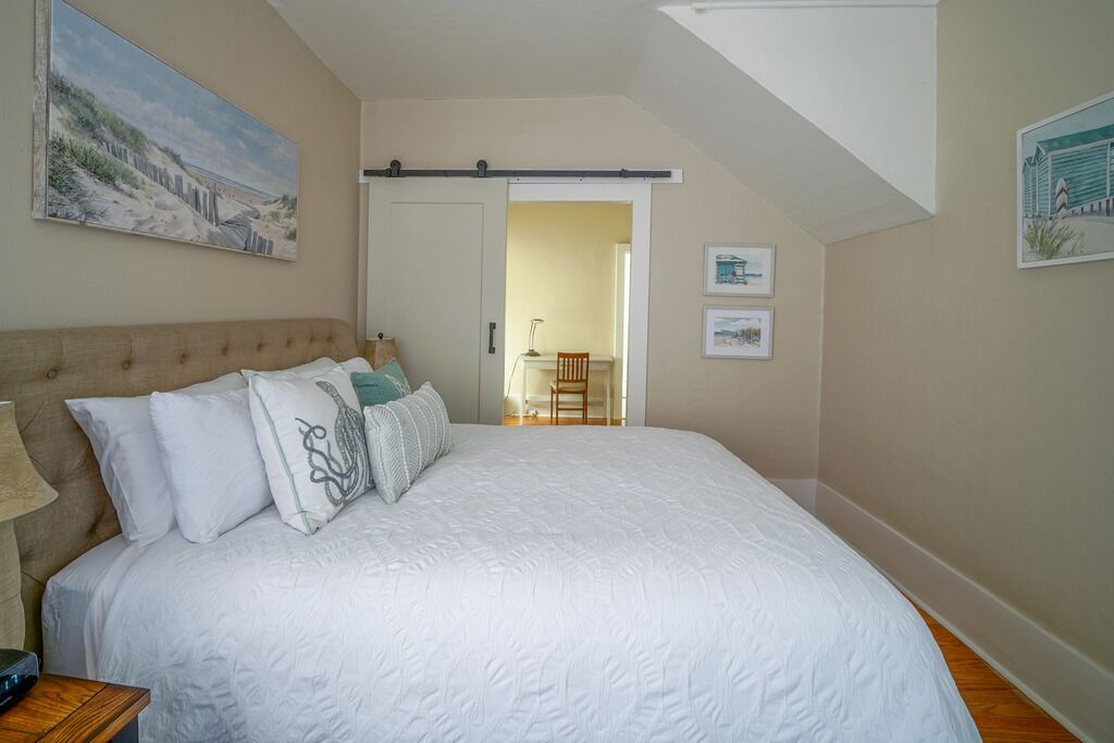 A bedroom with a large bed, a nightstand, a sliding door, and a painting on the wall.