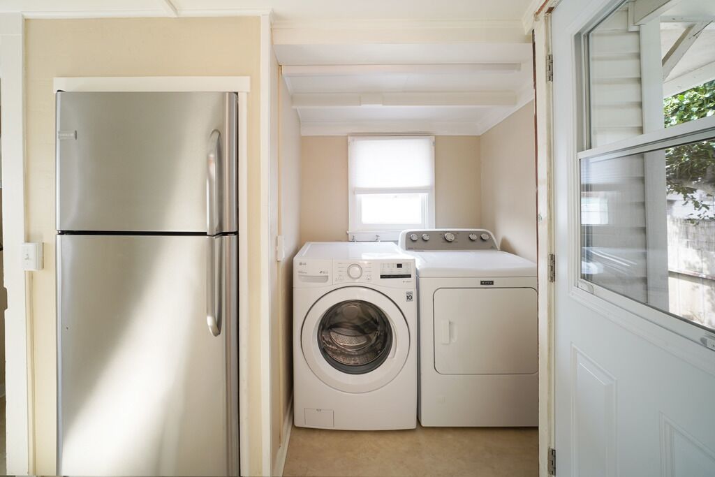 Un lavadero pequeño con un refrigerador de acero inoxidable, lavadora de carga frontal y secadora apilada.