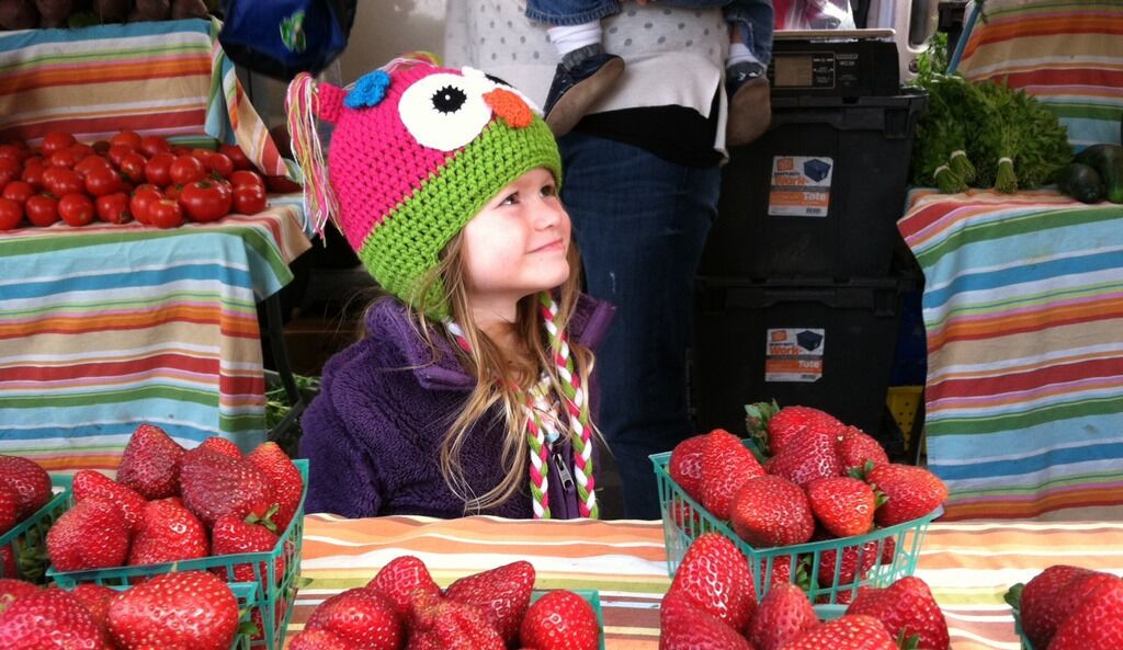 A person at a market stall with baskets of strawberries and tomatoes.