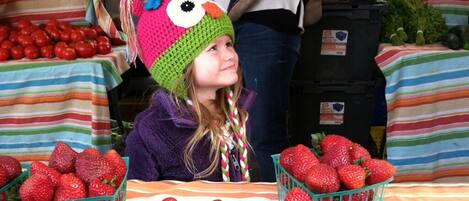 A person at a market stall with baskets of strawberries and tomatoes.