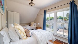 A bedroom with a large window, a bed with white bedding, a nightstand, and a ceiling light fixture. - Saltbox - Pacific Grove House - Two Blocks to Beach and Downtown! (Pacific Grove)