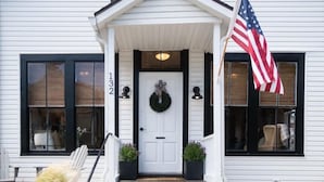 A white building with a front porch, a door with a wreath, and an American flag. - Saltbox - Pacific Grove House - Two Blocks to Beach and Downtown! (Pacific Grove)