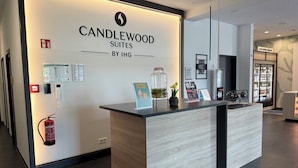 A reception desk with a sign for Candlewood Suites by IHG, a fire extinguisher, a phone, and a small potted plant. - Candlewood Suites Berlin Charlottenburg by IHG (Berlin)