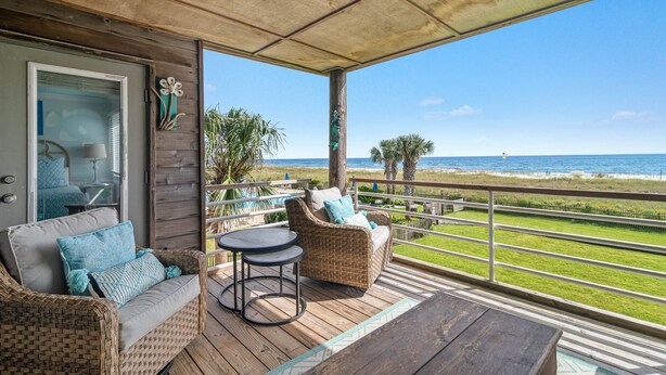 Un espace extérieur abrité avec des meubles en osier, une vue sur la plage et une terrasse en bois.