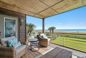 A covered outdoor seating area with wicker furniture, a view of the beach, and a wooden deck.