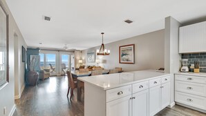 A modern kitchen with white cabinetry, a large island, and a dining area with a view. - Needle Rush Point A24 | Walk to FloraBama | 2 Pools | 2 Boat Docks w/Slips | My Beach Getaways (Pensacola)