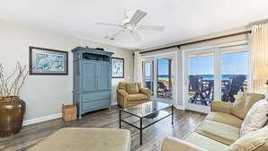 A living room with a glass coffee table, beige sofas, a blue cabinet, and a ceiling fan. - Needle Rush Point A24 | Walk to FloraBama | 2 Pools | 2 Boat Docks w/Slips | My Beach Getaways (Pensacola)