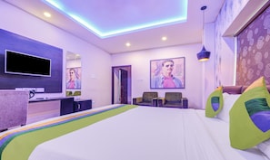A modern hotel room with a large bed, a flat-screen TV, a desk, and two chairs. - Treebo The Bollywood (Bhubaneshwar)