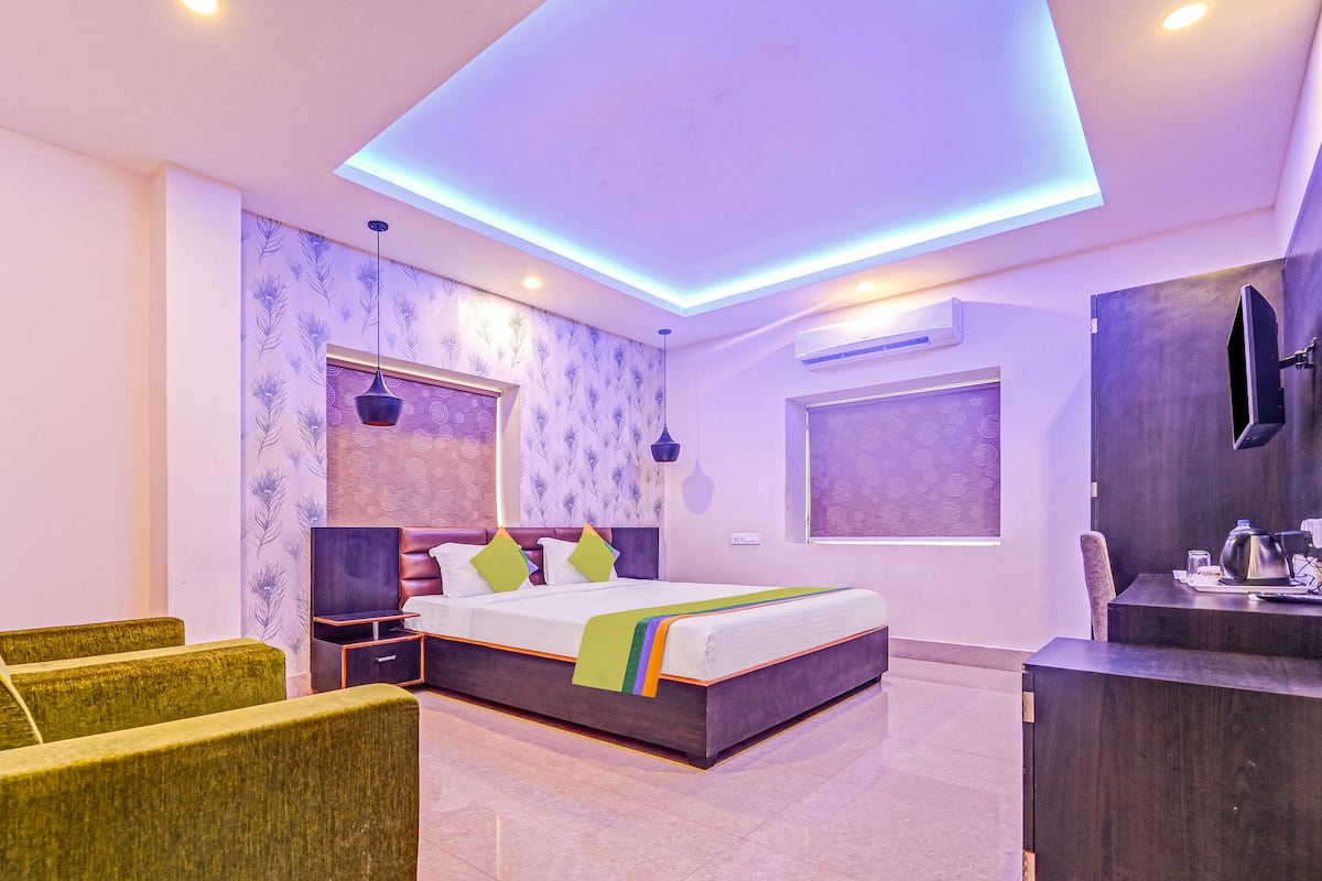 A modern bedroom with a large bed, green upholstered chairs, a desk, and a TV.