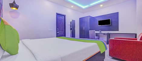 A modern hotel room with a bed, a desk, a chair, and a TV mounted on the wall.