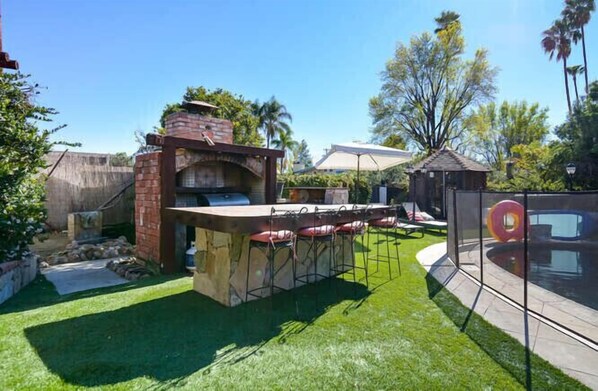 An outdoor barbecue area with a stone oven, a bar counter, and a pool.