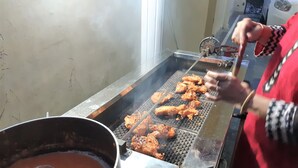 Uma pessoa grelhando asas de frango em uma churrasqueira portátil.