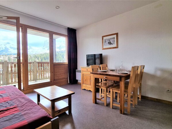 Una habitación con cama, una mesa de comedor con sillas, televisión y ventana con vista a montañas.