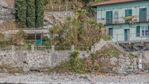 Un muro de piedra con un cuerpo de agua al frente, un edificio con balcón y una escalera que conduce al edificio.