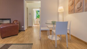 Una sala de estar moderna con un sofá de cuero, una mesa de comedor de vidrio con sillas blancas, una lámpara de pie y obras de arte en la pared.