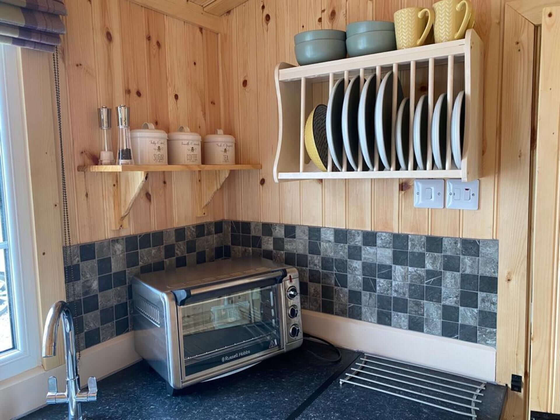 A kitchen with a built-in toaster oven, wooden shelves with kitchenware, and a tiled backsplash.