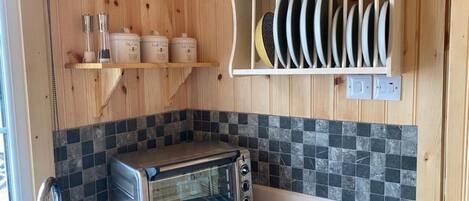 A kitchen with a built-in toaster oven, wooden shelves with kitchenware, and a tiled backsplash.