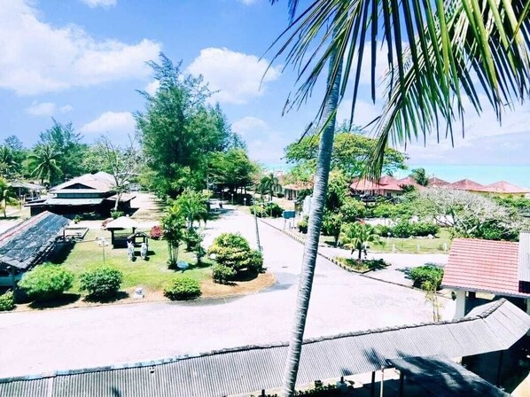 A resort area with a paved walkway, palm trees, and buildings with red roofs. - PCB Beach Resort (Kota Bharu)