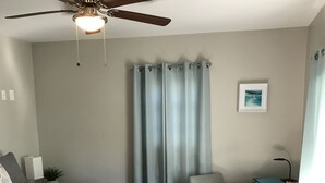 Ein Schlafzimmer mit einem Bett, einem Schreibtisch, zwei Stühlen, einem Deckenventilator und einem kleinen Tisch mit einer Lampe.