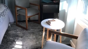 Ein Hotelzimmer mit einem Bett, zwei Stühlen, einem kleinen Tisch mit einem Buch, einem Schreibtisch mit einer Lampe und einem gerahmten Bild an der Wand.