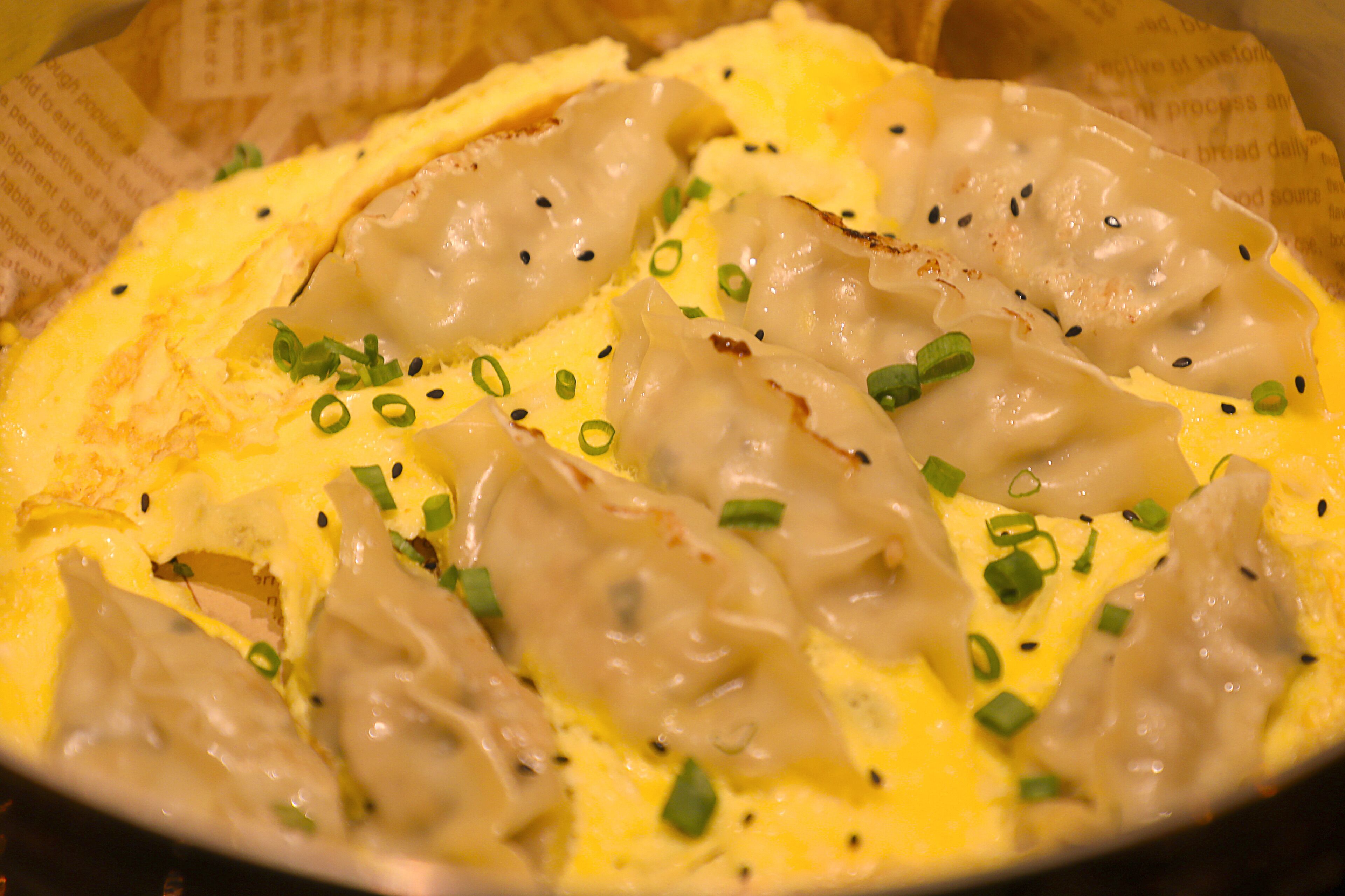 A dish with dumplings on a bed of scrambled eggs, garnished with green onions and black sesame seeds.