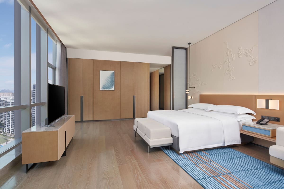 Quarto de hotel moderno com uma cama grande, televisão, escrivaninha e vista para a cidade.