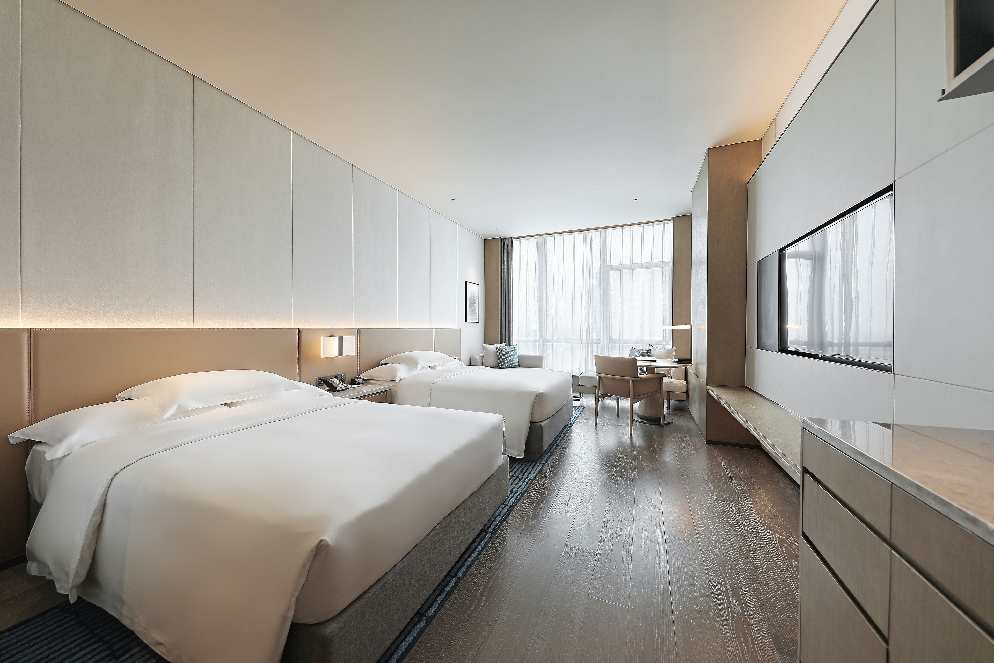 A modern hotel room with two beds, a desk, and a large window.