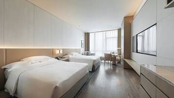 A modern hotel room with two beds, a desk, and a large window.
