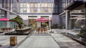 Un espacio exterior moderno con una zona de estar, una fuente de agua y plantas en macetas.