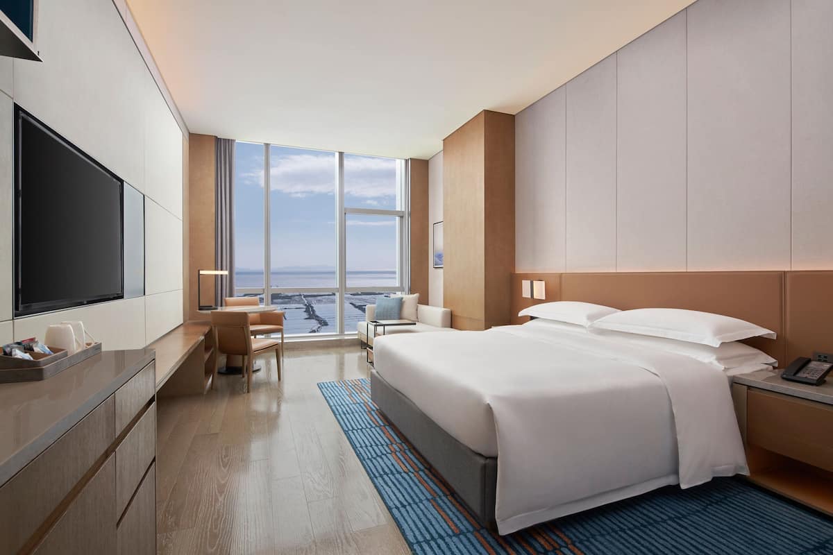 Quarto de hotel com uma cama grande, uma escrivaninha, uma televisão e vista para o oceano.
