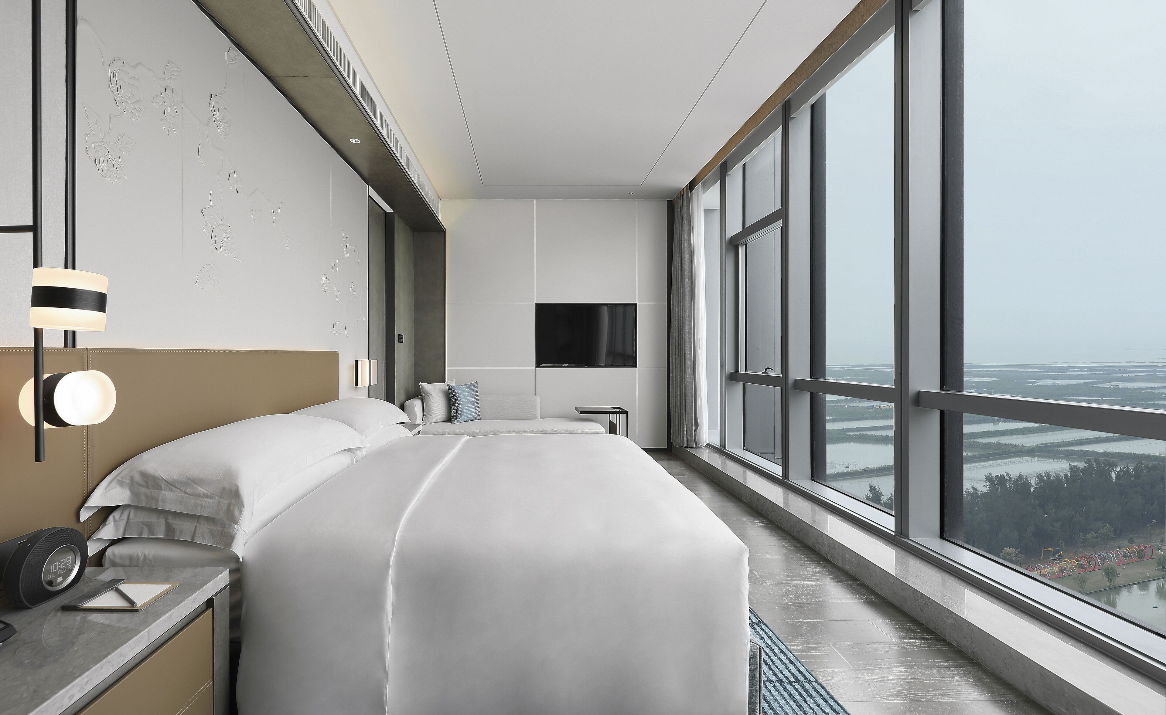 Un hotel moderno con una cama grande, un televisor montado en la pared y vistas a la ciudad a través de amplias ventanas.